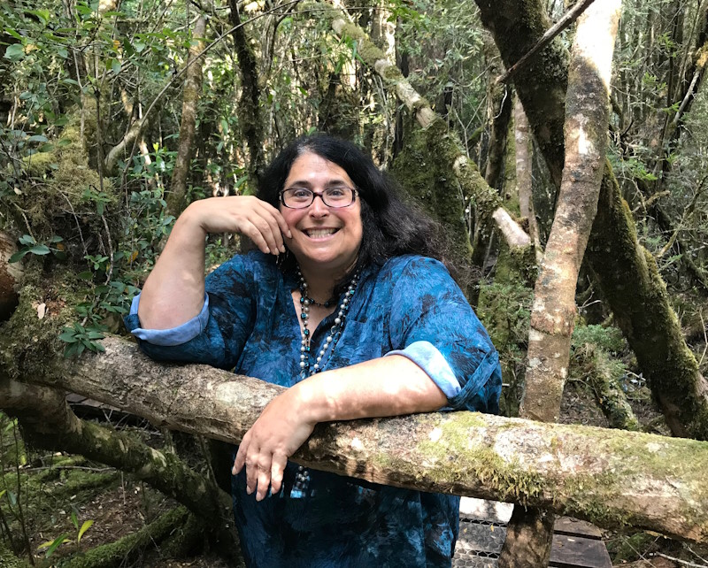 Lisa-an gershwin is stood in a wood and smiling at the camera wearing a denim shirt.