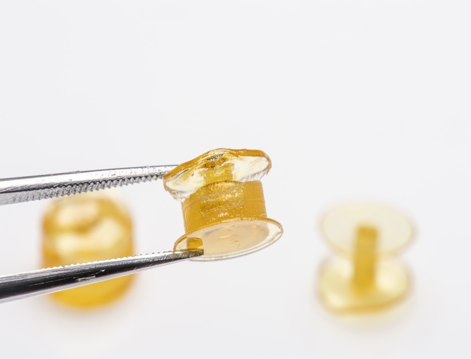 tweezers hold a yellow pill with two others out of focus