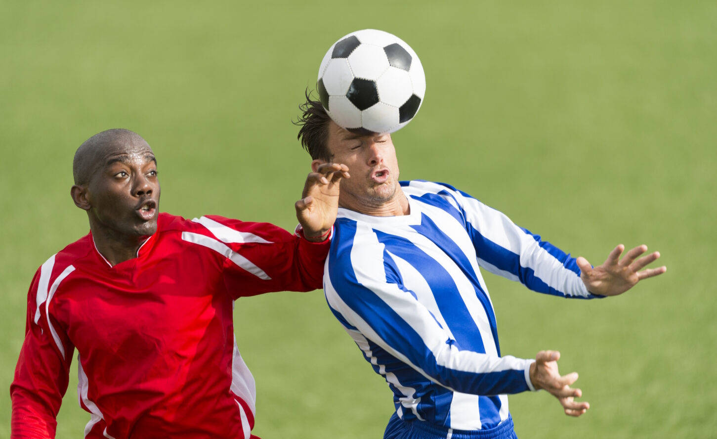 A footballer hits a ball with his head next to an opponent