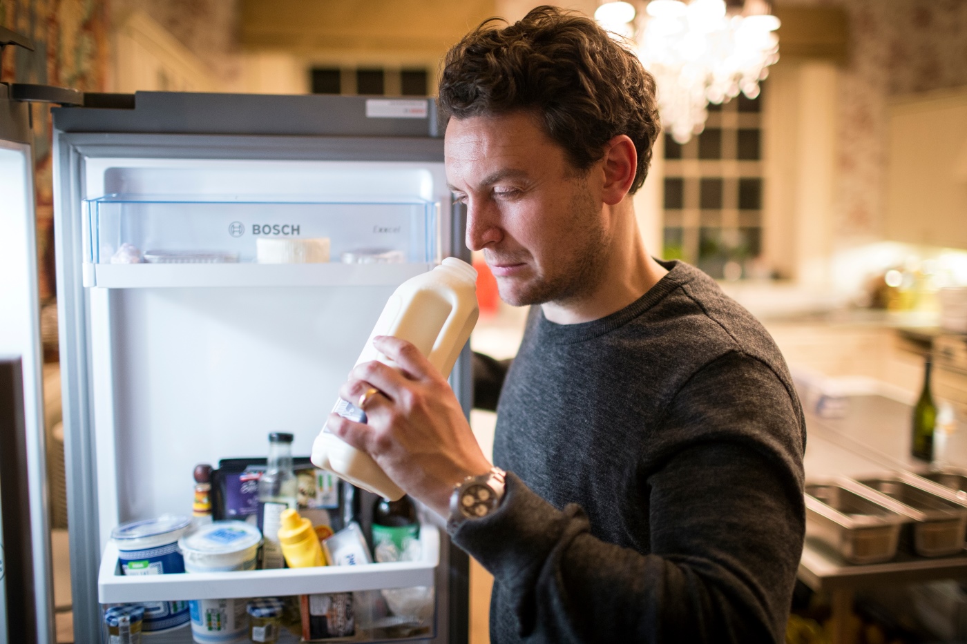A man smelling a carton of milk from his fridge to work out whether it has expired