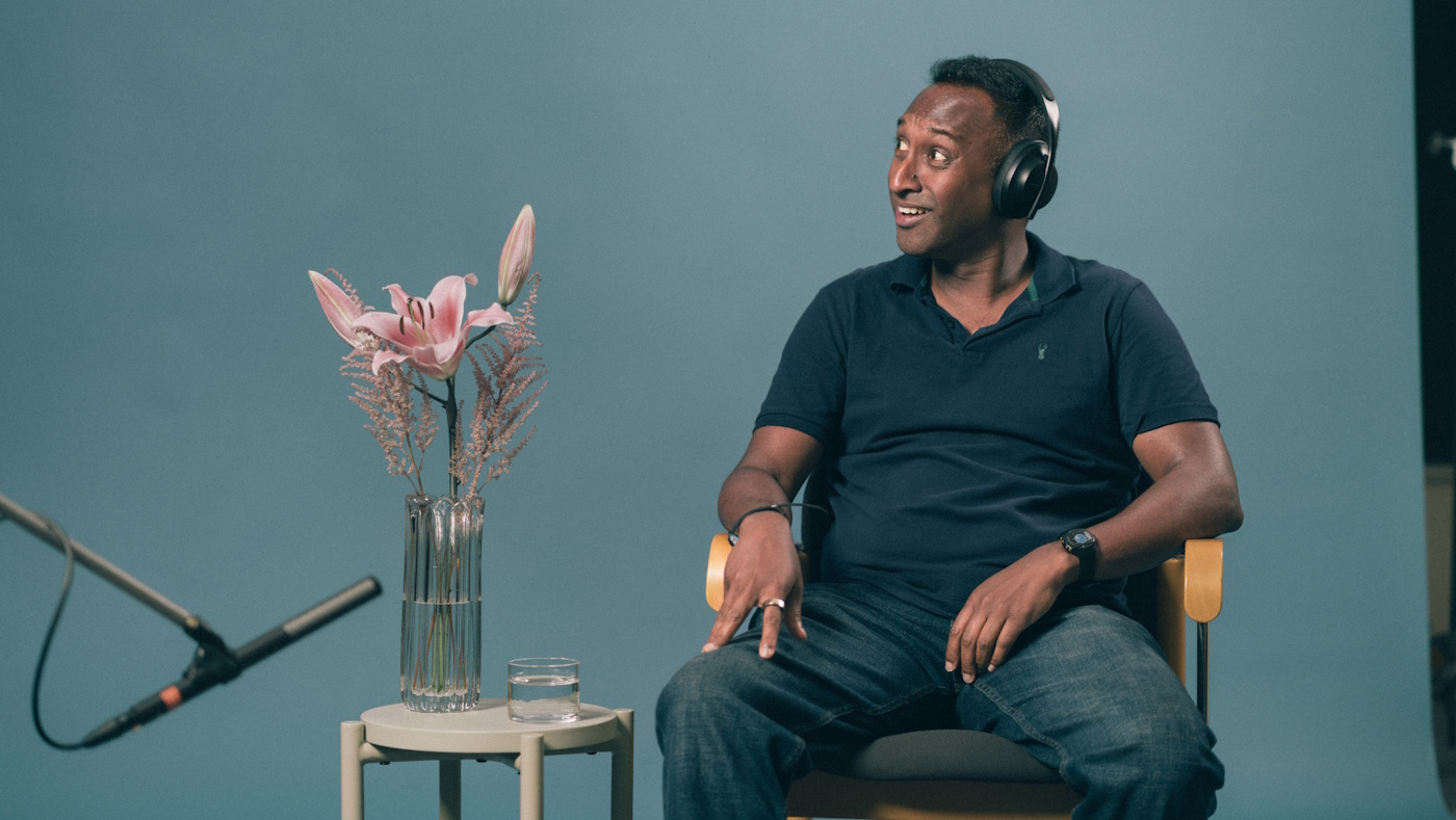 A man wearing headphones sits next to a vase with flowers