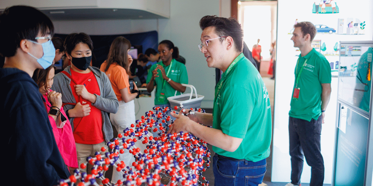 Exhibitor talking to members of the public with a large model molecule on the table between them